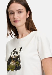 Weißes Baumwoll-T-Shirt mit einem Motiv eines Pandas, der eine Brille und Schmuck trägt und Bambus hält. Rundhalsausschnitt und kurze Ärmel.