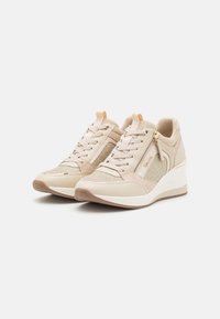 Beige sneakers met een gestructureerde bovenkant, vetersluiting aan de voorkant en een ritsdetail aan de zijkant. Witte wigzool met een subtiele bruine buitenzool.