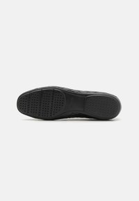 Svart såle med teksturert grep mønster og ventilasjonshull. Har glatte kanter og merkevare på undersiden.