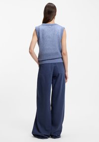 Blauer gestrickter ärmelloser Pullover mit rundem Ausschnitt und geripptem Saum, kombiniert mit weiten marineblauen Hosen mit Details an den Gesäßtaschen.