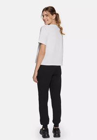 Witte katoenen t-shirt met korte mouwen, gecombineerd met zwarte joggingbroek. De outfit heeft een losse pasvorm en elastische boorden bij de broek.