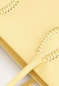 Gelbe Lederhandtasche mit aufwendigen gestickten Akzenten entlang der Oberseite, flaches Design und zwei Tragehenkel für eine einfache Handhabung.