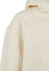 Lys beige, teksturert hettegenser med stor hette og avslappet passform, laget av et mykt og behagelig stoff.