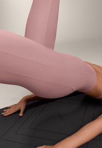 Ružové legíny s vysokým pásom s rebrovanou textúrou, priliehavým strihom a bezšvovými detailmi, v kombinácii s čiernou textúrovanou jógovou podložkou.