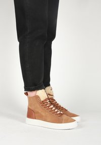 Ruske nubuk høghælede sko med fuskepelsfor, med hvide gummisåler og brune snørebånd, parret med sorte jeans.