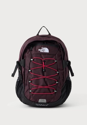 Sac à dos violet foncé et noir avec des cordons élastiques rouges à l'avant, des poches en mesh sur les côtés, et le logo "The North Face" sur le panneau avant supérieur.