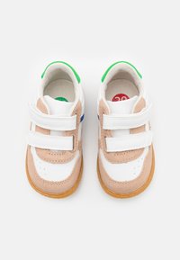 Baskets blanches et marron clair avec des bandes Velcro, semelles en caoutchouc et accents colorés en vert, bleu et rouge. Matériaux en daim et en synthétique.