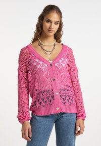 Cárdigan rosa de punto abierto con escote en V, mangas largas y corte amplio. Presenta botones decorativos y un patrón texturizado. Combinado con denim.