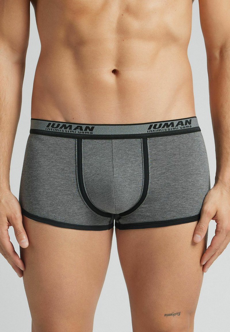 Grijze boxershorts van zachte stof, met een zwarte elastische tailleband met merknaam, en contrasterende zwarte afwerking langs de pijpen.