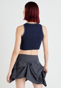 Top cropped canelado azul-marinho com acabamento branco em contraste, combinado com uma saia cinza com detalhes pregueados e uma ampla cintura elástica.