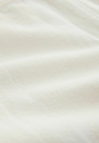 Tissu doux blanc cassé avec une texture subtile côtelée en diagonale et des plis délicats.