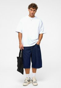 Witte oversized t-shirt, donkere spijker bermuda shorts, zwarte tote bag, witte sokken en sneakers. Eenvoudig ontwerp met een relaxte pasvorm en casual stijl.