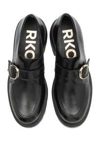 Un paio di mocassini neri in pelle con fibbie dorate e la scritta "RIKO" stampata in oro all'interno delle scarpe, visti dall'alto su uno sfondo bianco.