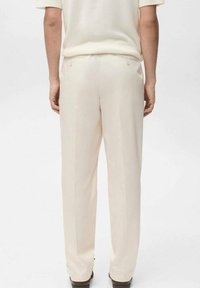 Beżowe spodnie na miarę o gładkiej teksturze, z prostymi nogawkami, dwoma tylnymi kieszeniami i subtelnymi detalami przeszyć.