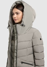 Kurtka puchowa w jasnoszarym kolorze z dużym kapturem. Pikowany design, zamek błyskawiczny z przodu oraz boczna kieszeń na zamek. Gładka tekstura, wodoodporny materiał.