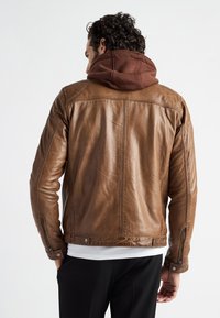 Ruskea nahkatakki, jossa on istuva muotoilu, ruskea huppu ja sivuvetoketjut. Sileä pinta, jossa on näkyviä ompeluyksityiskohtia.