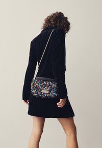 Blizganti per petį nešiojama rankinė iš daugių spalvų žvynelių su juodos odos viršumi, sidabriniu grandinėlės dirželiu ir stačiakampio formos metaliniu akcentu.