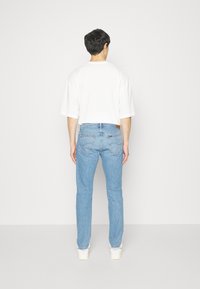 Jeans azul claro con un corte clásico, que cuentan con cinco bolsillos y una etiqueta de cuero en la parte posterior. Combinados con una camiseta blanca de corte oversized.