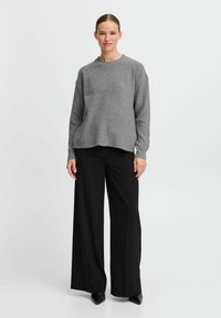 Maglione grigio chiaro a coste con scollo rotondo, abbinato a pantaloni neri a vita alta a gamba larga e scarpe nere con punta.