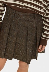 Brown herringbone skirt with pleats and blue flecks, made of textured fabric. Featuring a mid-rise waistband and a tailored fit.