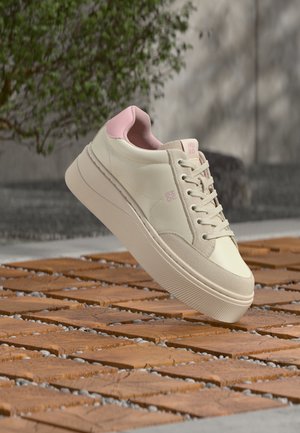Κρεμ και ροζ sneakers με πλατφόρμα, κορδόνια και λογότυπο Hugo, αιωρούμενα πάνω από ξύλινη και πέτρινη εξωτερική επιφάνεια.