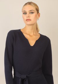Maglione a collo a V di colore blu navy con maniche lunghe, caratterizzato da una cintura da annodare in vita e una texture morbida. Design semplice ed elegante senza motivi.