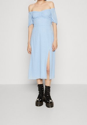 Helles blaues schulterfreies Kleid mit kurzen Puffärmeln, gerafftem Oberteil, knie-langer Länge und einem seitlichen Schlitz, kombiniert mit schwarzen Schnürstiefeln.