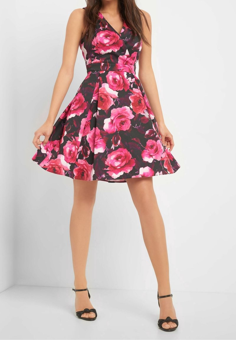 Květinové šaty s růžovými růžemi na černém pozadí, silueta ve tvaru písmena A, výstřih do V a délka ke kolenům. V kombinaci s černými sandály na vysokém podpatku.