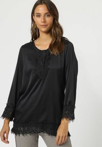 Blusa de satén negra con mangas largas, un borde de encaje en el escote y los puños, y una serie de botones en la parte delantera. Textura suave.