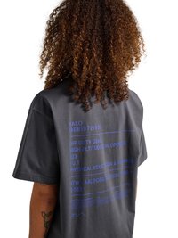 Persoon met krullend haar die een donkergrijs T-shirt draagt met blauwe bedrukte tekst op de achterkant over uitrusting buiten dienst en lichamelijke opvoeding.
