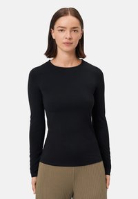 Dlouhý rukáv černého topu vyrobeného z hladké, elastické tkaniny s kulatým výstřihem a přiléhavým střihem. Spárováno s strukturovanými, žebrovanými béžovými kalhotami.