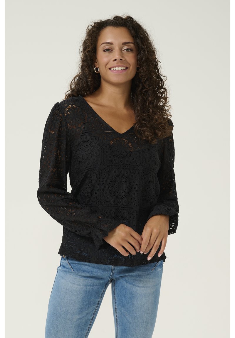 Blusa nera in pizzo con scollatura a V, maniche lunghe a sbuffo e motivi floreali. Abbinata a jeans in denim azzurro chiaro. Tessuto testurizzato.