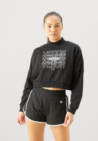 Sweatshirt noir court avec un graphique "VENUM" blanc, doté d'un col haut. Associé à un short noir, avec des bordures blanches et un logo sur la ceinture.
