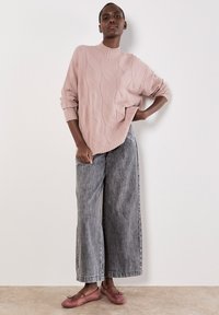 Hellrosa, strukturierter Oversize-Pullover mit geripptem Kragen; kombiniert mit weit geschnittenen, ausgewaschenen grauen Jeans und rosa Ballerinas.