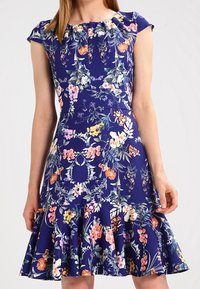 Blomtryckt klänning med marinblå bakgrund, korta ärmar, plisserad halsringning och utställd nederdel med volangdetalj. Slät tygkvalitet.
