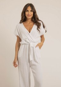 Combinaison blanche texturée avec un décolleté en V et des manches courtes, dotée d'une ceinture à nouer à la taille et de pantalons larges et fluides.