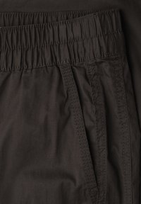 Czarne spodnie z elastycznym pasem, boczną kieszenią i widocznym przeszyciem na lekkiej tkaninie.