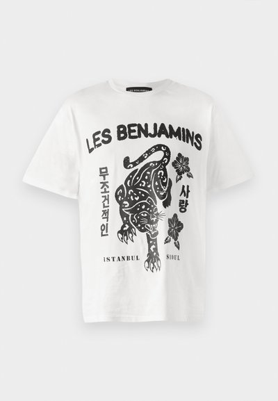 T-shirt en coton blanc avec un graphisme noir représentant un jaguar, des fleurs et du texte en plusieurs langues. Col rond et manches courtes.