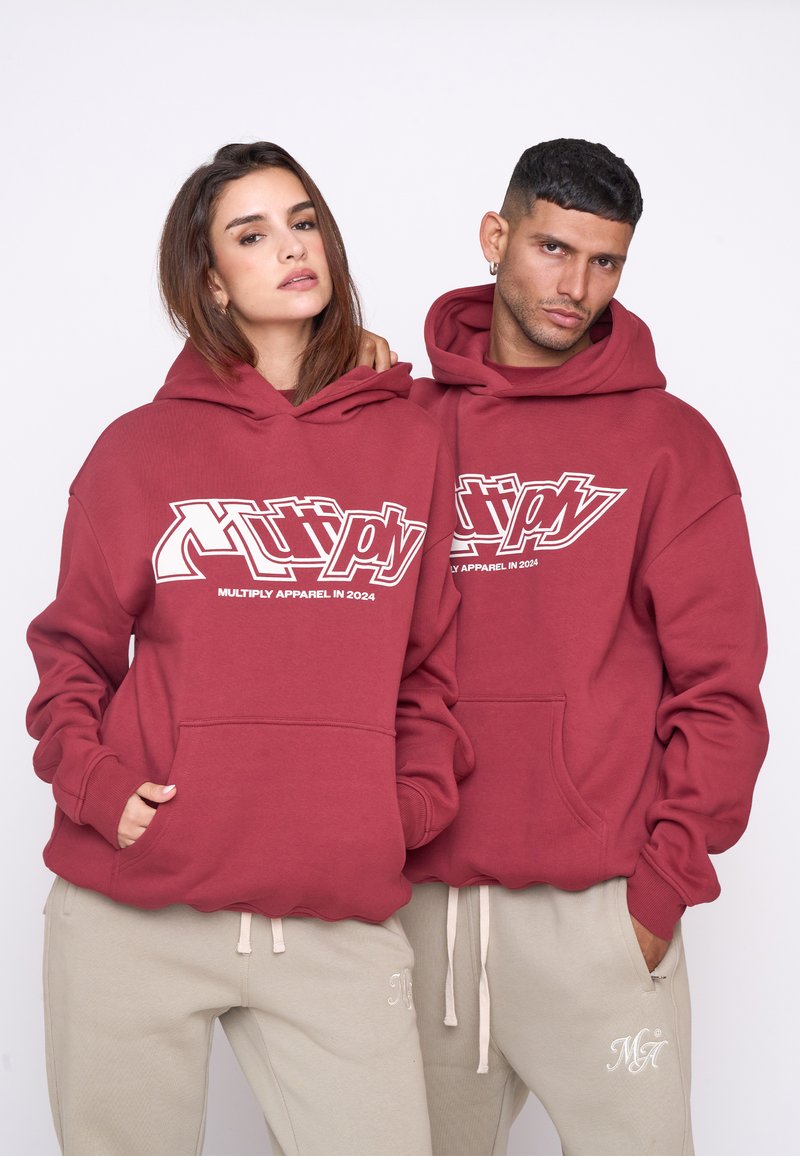 Hanorace maronii cu o mare grafică albă "Multiply Apparel in 2024"; material din amestec de bumbac; buzunare frontale; asortate cu pantaloni de trening bej.
