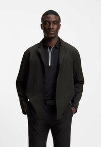 Svart pikétröja med vit accent, lager av en svart lätt jacka. Outfiten har smalnande svarta byxor och ett synligt bälte.
