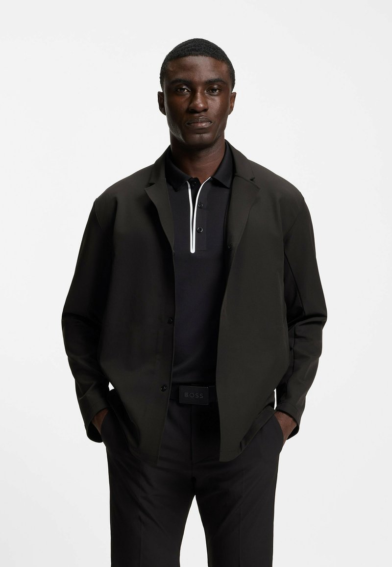 Svart pikétröja med vit accent, lager av en svart lätt jacka. Outfiten har smalnande svarta byxor och ett synligt bälte.