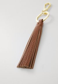 Porte-clés en cuir brun avec une finition texturée, doté d'un fermoir et d'un anneau en métal de couleur dorée. Les brins de la frange sont allongés et effilés.