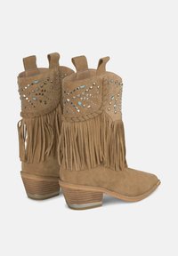 Botas cowboy de ante marrón con detalles de flecos, tachuelas metálicas y un tacón de varias capas. Presentan una punta redondeada y bucles en la parte superior para ponerlas fácilmente.