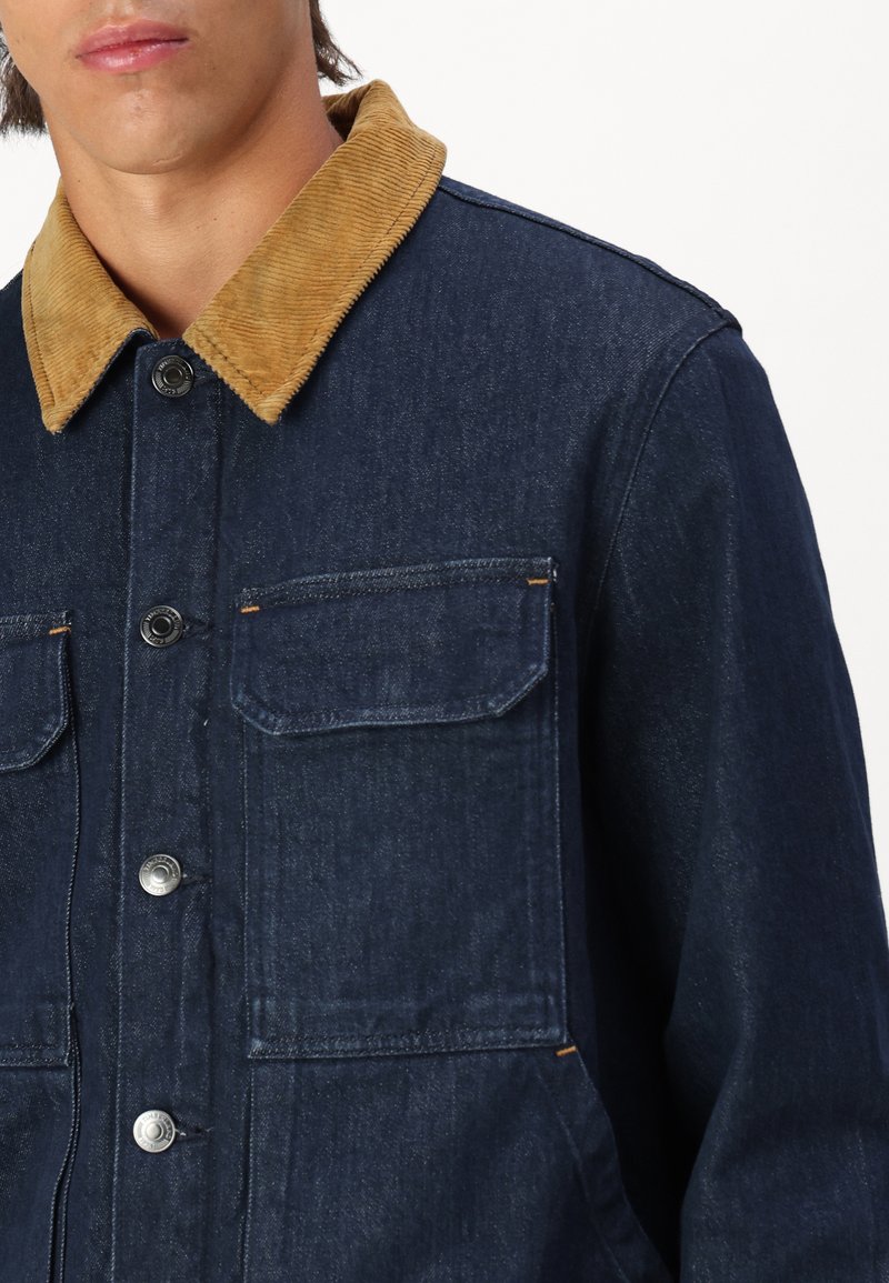 Czarna dżinsowa kurtka z kontrastowym kołnierzem z materiału sztruksowego, zatrzaskami, dwoma kieszeniami na piersi i detalami w pomarańczowym kolorze.