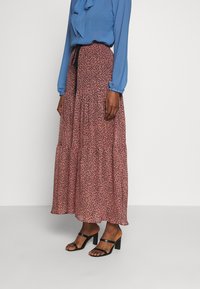 Blouse bleue avec un col à volants, associée à une longue jupe rose à volants avec un imprimé léopard noir éparpillé, et des sandales à talons noires.