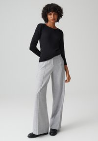 Maglietta nera a maniche lunghe a costine abbinata a pantaloni larghi grigio chiaro. I pantaloni presentano cuciture verticali e un sottile motivo testurizzato.