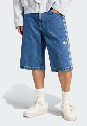 Denim-Cargo-Shorts mit entspanntem Schnitt, blauer Farbe und weißem Adidas-Logo. Getragen mit weißen Sneakern und gerippten weißen Socken.