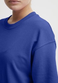 Blå sweatshirt lavet af en bomuldsblanding, med en ribbet rund halsudskæring, sænkede skuldre og en glat overflade.
