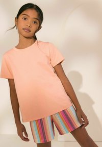 Helles rosa Baumwoll-T-Shirt mit kurzen Ärmeln, kombiniert mit mehrfarbigen gestreiften Shorts, die vertikale Linien in verschiedenen Pastelltönen zeigen.