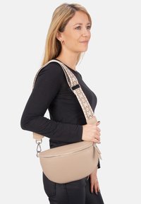 Beige Leder Umhängetasche mit einer strukturierten Oberfläche, ausgestattet mit einem gemusterten verstellbaren Riemen und einem Reißverschluss.